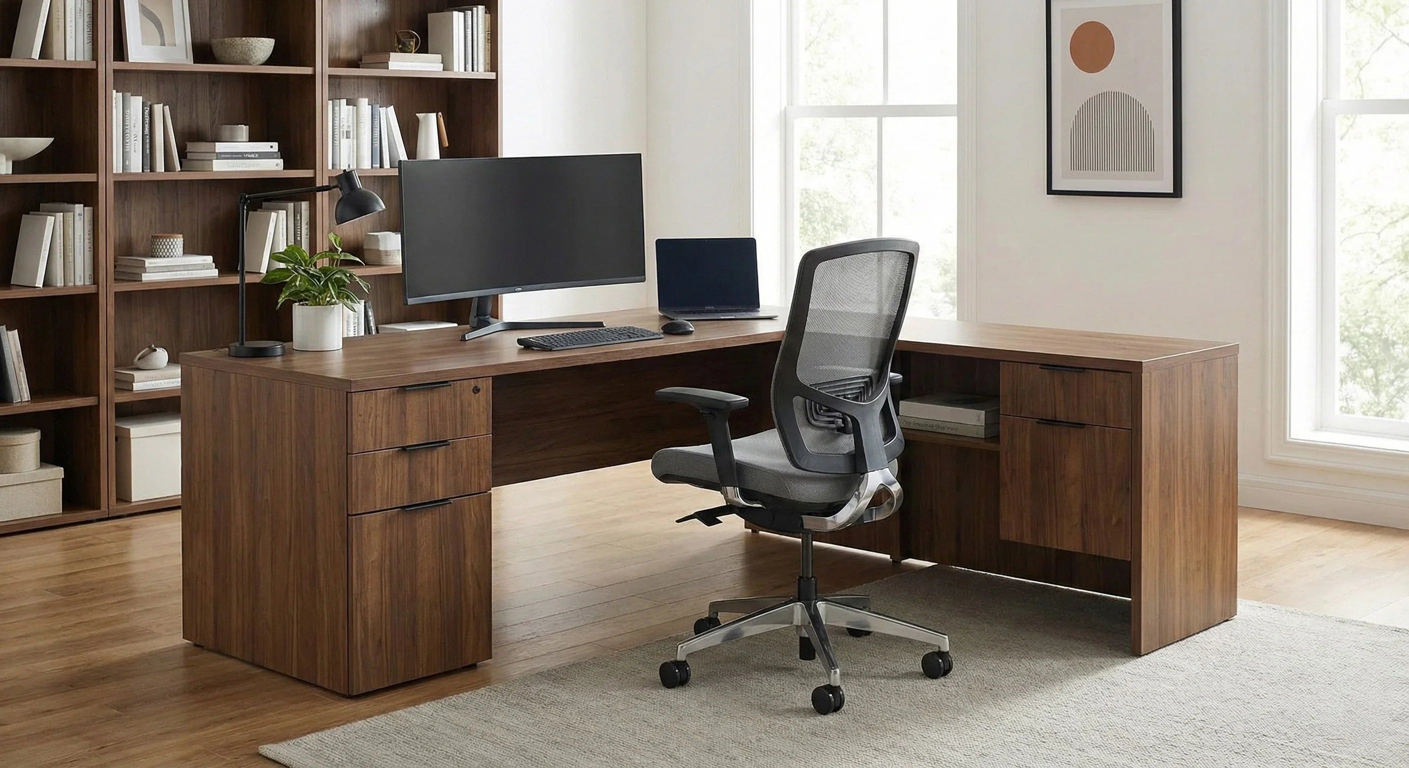 Modern home office with L-shaped wood desk, ergonomic chair, large monitor, and bookshelf
