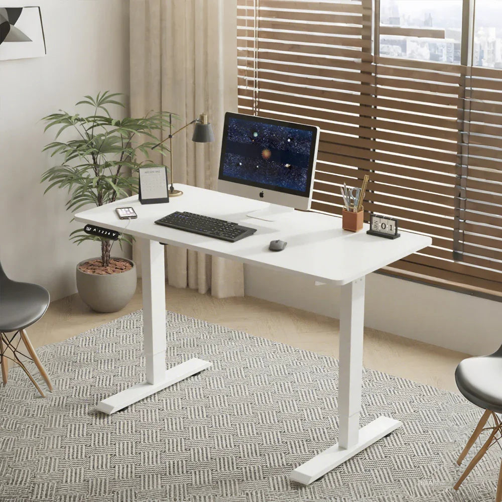 Modern home office with white height-adjustable desk, computer, and minimalist decor