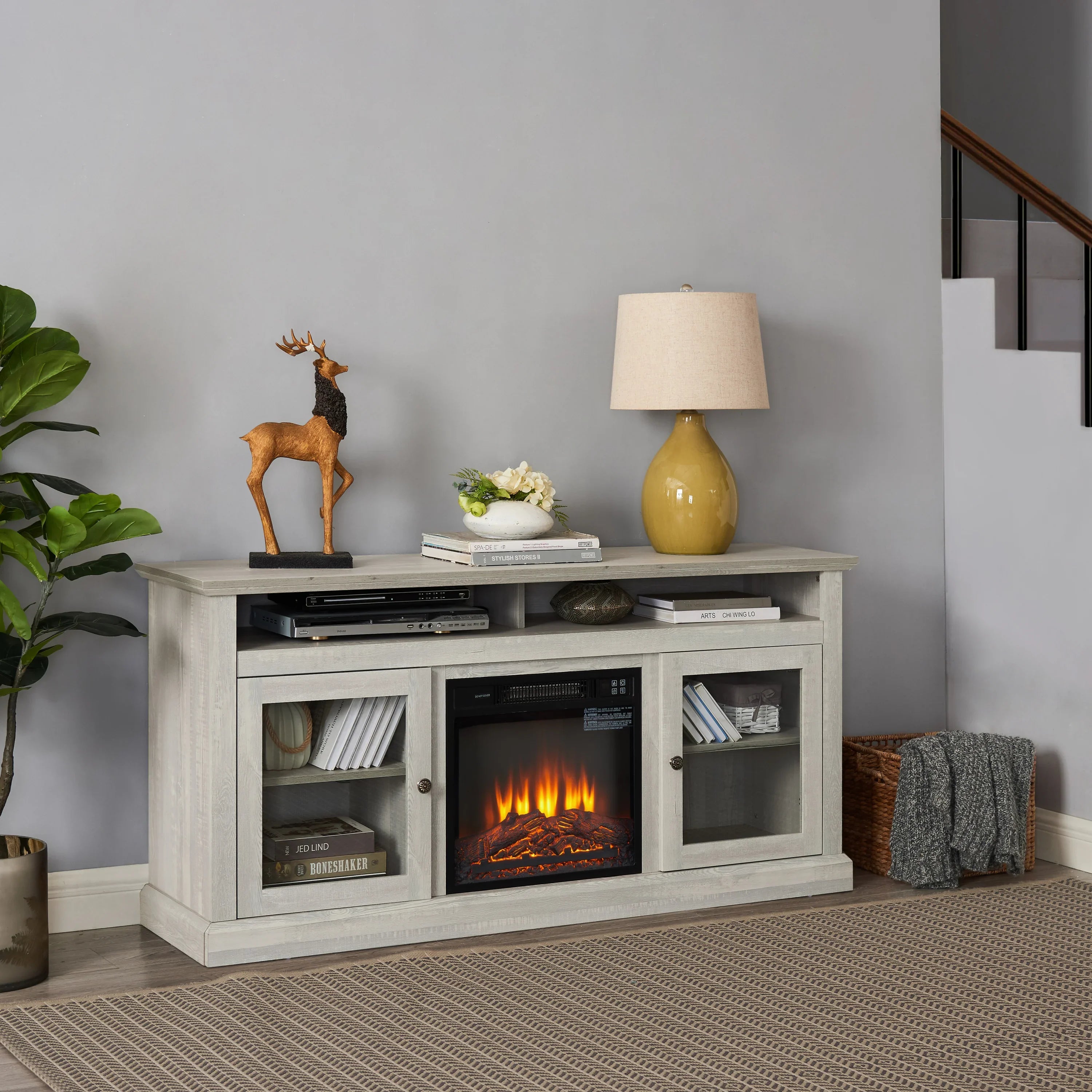 Modern living room with white TV console, electric fireplace, decor lamp, and accent plant