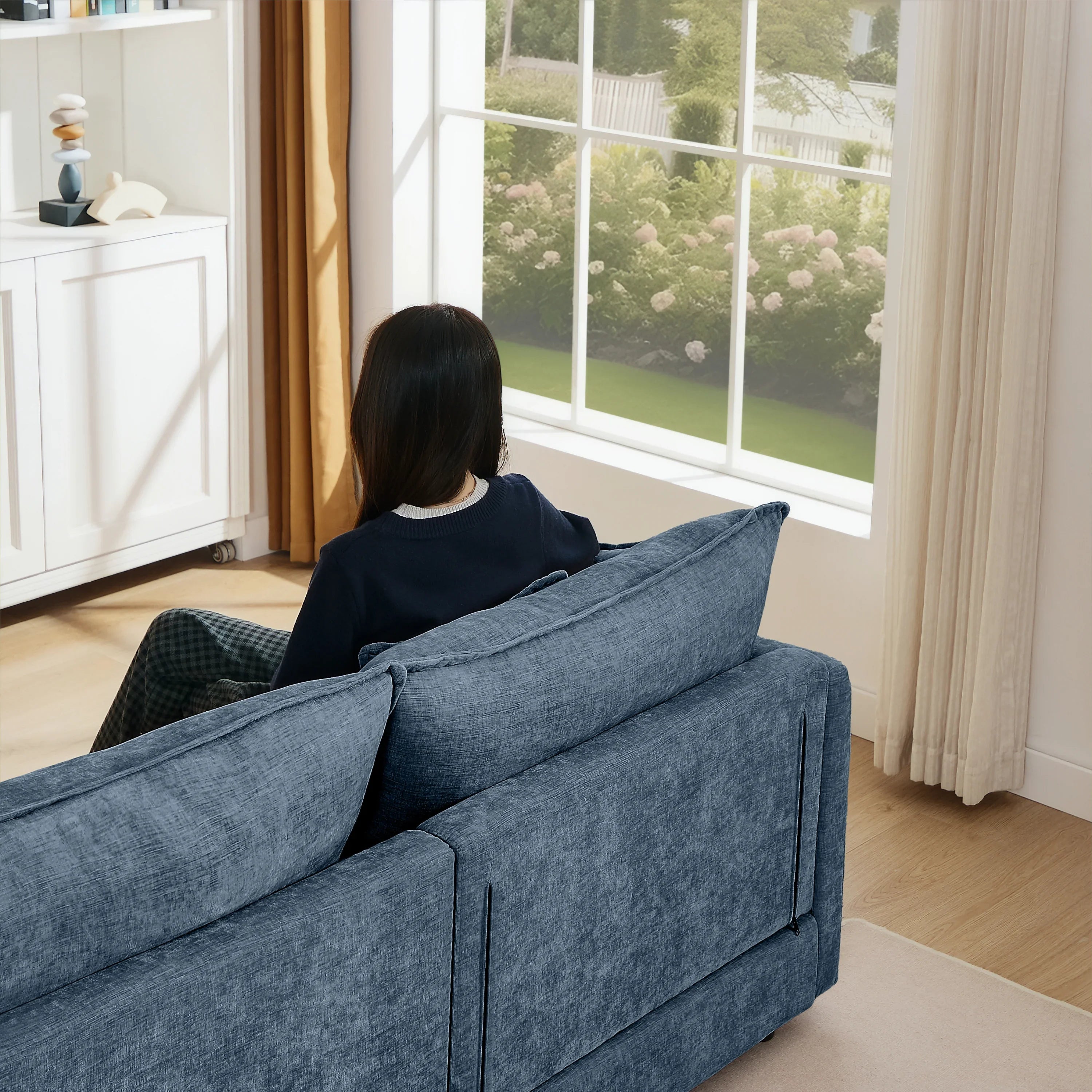 Woman sitting on blue modern sectional sofa by large window in bright living room